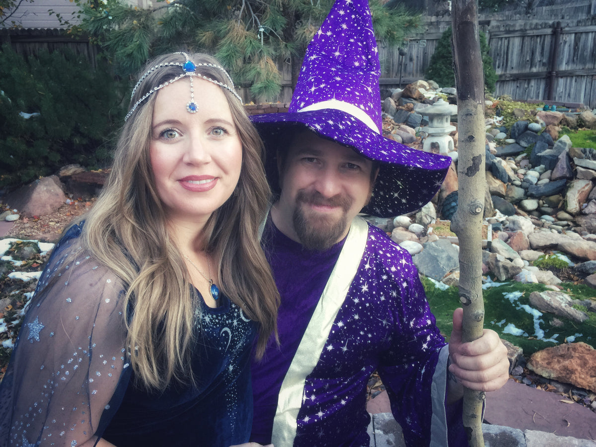 A man and woman posing in a purple wizard and starry night costume set outdoors in front of a rocky garden background.